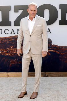 an older man in a tan suit and white shirt standing on the red carpet with his hands in his pockets