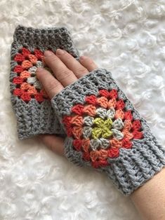 a hand is holding onto a crocheted gray and orange mitt on a white surface