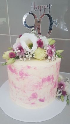 a pink and white cake sitting on top of a table next to a happy 90th birthday sign