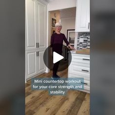 a woman standing in a kitchen next to white cupboards and an island with drawers