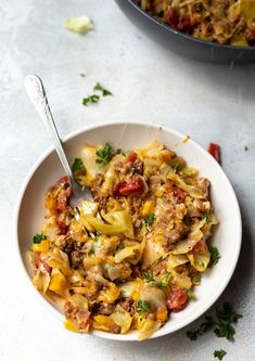 a white bowl filled with pasta and meat on top of a table next to a skillet