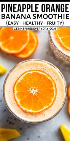 two glasses filled with orange banana smoothie on top of a gray table next to sliced oranges