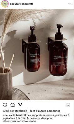 two soap dispensers sitting next to each other on a counter with a plant in the corner