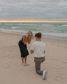 a man kneeling next to a woman on top of a sandy beach near the ocean