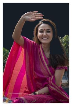 a woman sitting on top of a bench wearing a pink and orange sari with her hand in the air