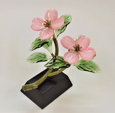 a vase with pink flowers in it sitting on a black base and green leaves around the stems