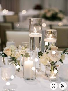 a table with candles and vases filled with white flowers on top of the table