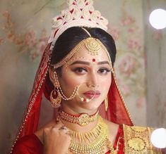 a woman wearing a red and gold bridal outfit with jewelry on her head, holding a candle in front of her face