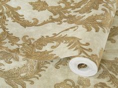 a roll of toilet paper sitting on top of a floral design wallpaper covered in gold and white fabric