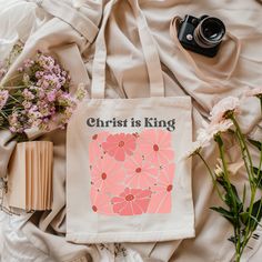 a tote bag with the words christ is king on it next to flowers and a camera