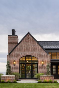 a brick house with large windows and a black door on the front porch is surrounded by green grass