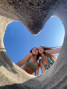 two girls are standing in the sand with their arms around each other and looking up at the sky