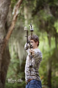 a young man is aiming his bow at the target in the woods while wearing glasses