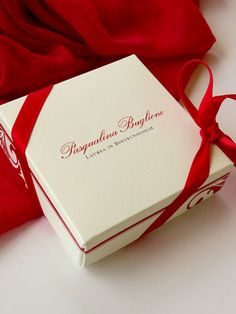 a white box with a red ribbon around it sitting on a table next to a red cloth