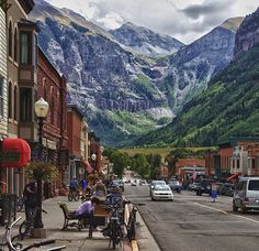 a city street with mountains in the background and people on bikes parked along the sidewalk