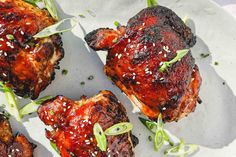 four pieces of meat on a plate with green garnishes and sesame seeds