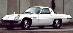 a white sports car parked in front of a concrete wall and green grass next to it