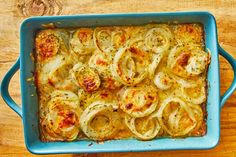 a blue casserole dish filled with onion rings on a wooden table, ready to be eaten