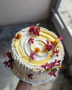 a hand holding a cake with white frosting and yellow icing decorated with flowers