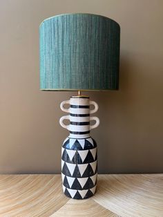 a black and white vase with a green shade on it sitting on a table next to a lamp