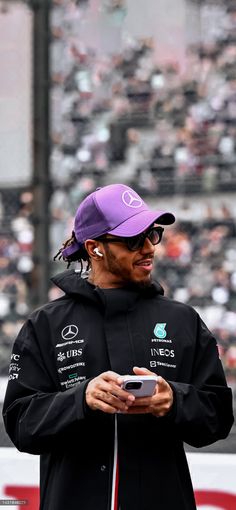 a man in a black jacket and purple hat looking at his cell phone while standing on a track