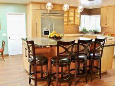 a kitchen island with four stools and a bowl of fruit on it