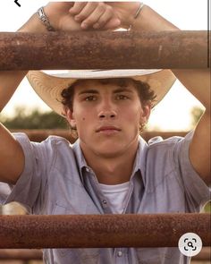 a young man wearing a cowboy hat and holding his hands on top of the bars