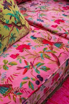 a pink floral couch with two pillows on it's back and one pillow sitting on top of it