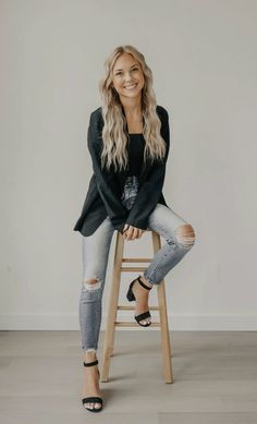 a woman sitting on top of a wooden stool wearing ripped jeans and black heels, smiling at the camera