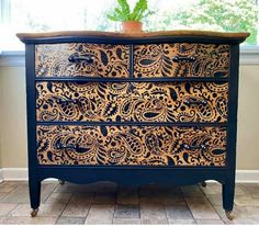 a black and gold painted chest of drawers in a room with tile flooring, potted plant on window sill