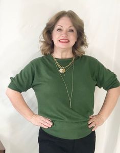 a woman standing with her hands on her hips wearing a green sweater and black pants