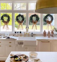 two wreaths on the kitchen counter in front of three windows with christmas wreaths hanging from them