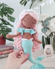 a crocheted little mermaid doll sitting on top of a table next to flowers