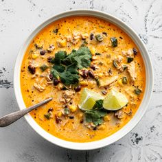 a white bowl filled with soup and garnished with cilantro, limes, and peanuts