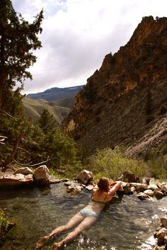 a woman laying down in the middle of a river with rocks and trees around her