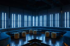 an empty room with blue couches and round tables in the center, lit by bright windows