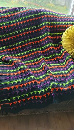 a crocheted blanket on a couch with a yellow pillow sitting next to it