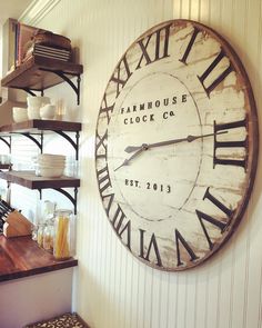 a large clock mounted to the side of a wall next to shelves filled with dishes