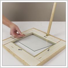 a person is holding a piece of wood with their hand over a square shaped frame