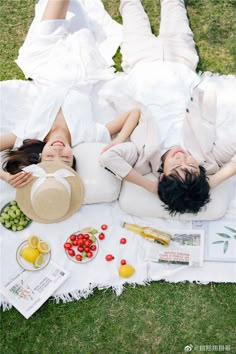 two women laying on the grass with food and drinks