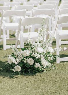 white chairs are set up in the grass for an outdoor ceremony with flowers and greenery