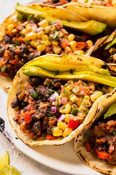 three tacos on a white plate with corn and avocado