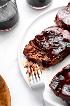 a white plate topped with ribs covered in bbq sauce next to a glass of wine