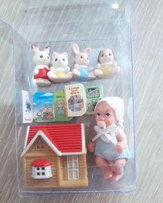 there is a small doll in the plastic case next to other toy animals and books