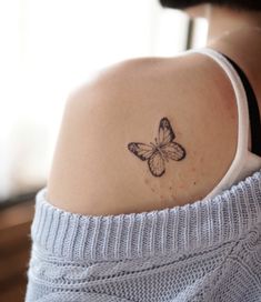 a woman with a small butterfly tattoo on her back shoulder is looking at the camera