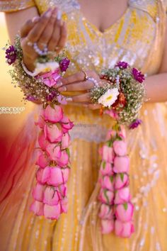 a woman in a yellow dress holding pink roses and greenery with her hands together