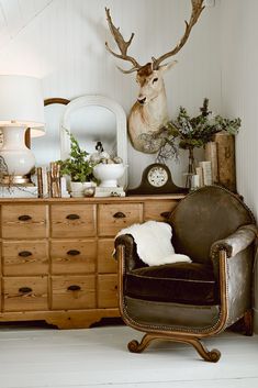 a chair sitting in front of a dresser with a deer head on top of it