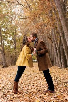 a man and woman are kissing in the park with leaves on the ground behind them