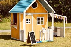 a small wooden house with a chalkboard sign next to it