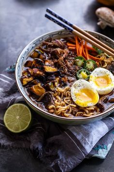 a bowl filled with noodles, eggs and vegetables next to chopsticks on a table